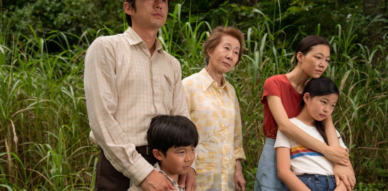 A family of five people stand in a wooded area.