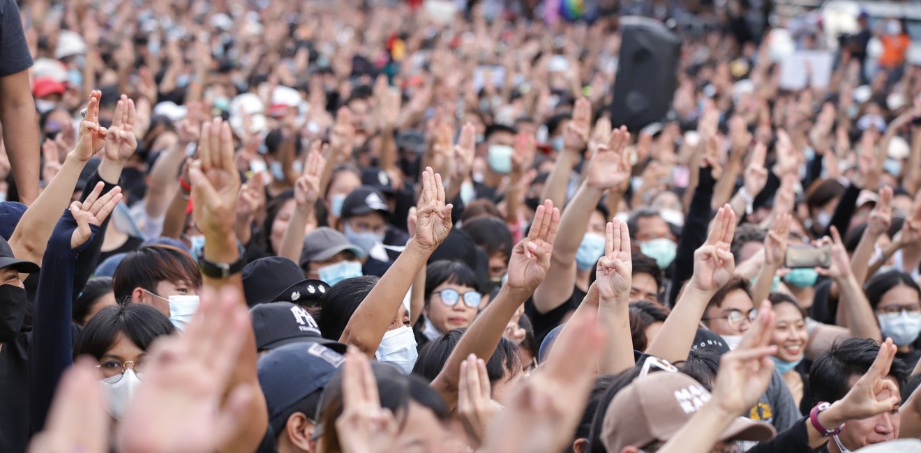 A crowd of people gathered at a protest, lifting their hands with three fingers extended in a gesture of protest against the government.