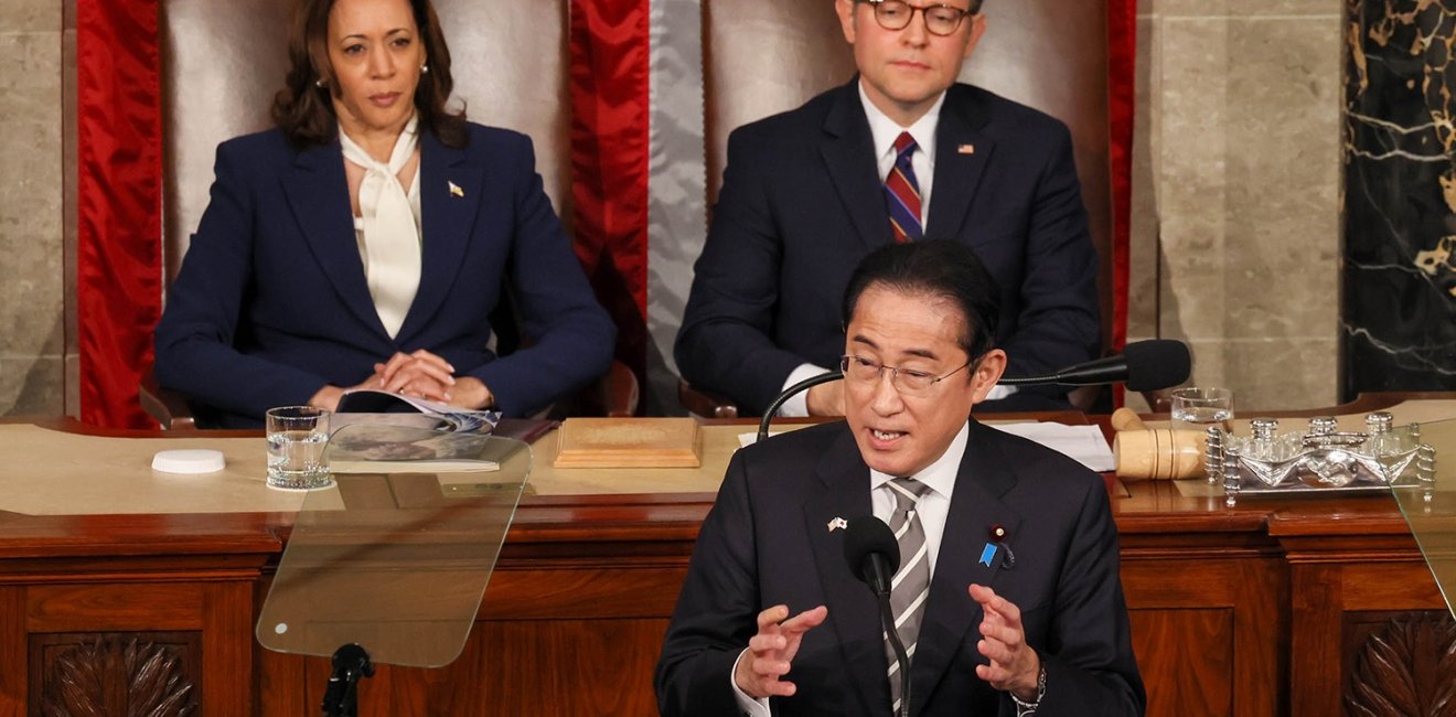 Prime Minister Kishida stands at a lecturn giving a speech, Vice President Harris and Speaker Johnson are seated behind him.