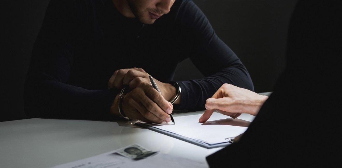  man with handcuffs signing a document in interrogation room