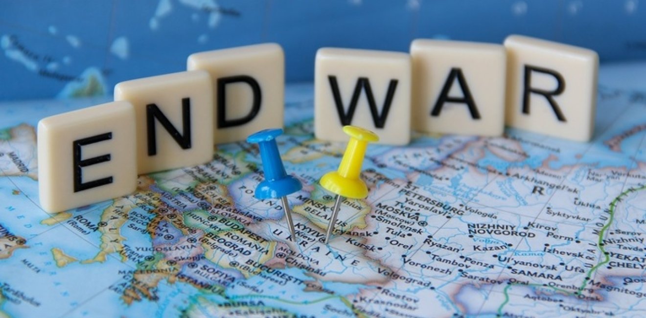 Low angle view of a sign that reads End War written with letter tiles behind yellow and blue Ukrainian flag colors push pins tacks pinned on Ukraine's map.