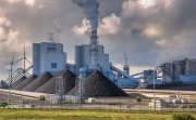 A large power plant with piles of coal outside of the buildings.