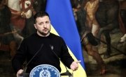 Volodymyr Zelensky standing in front of a Ukrainian flag and a painting of ancient warriors