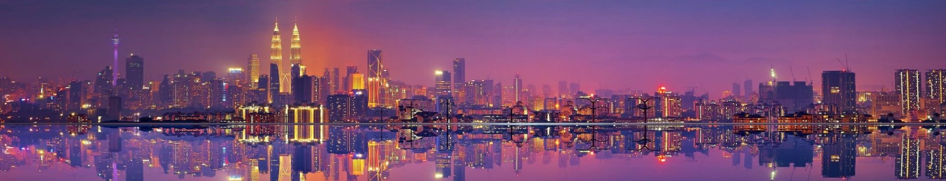 A panoramic shot of the city of Kuala Lumpur at night, seen from the water.