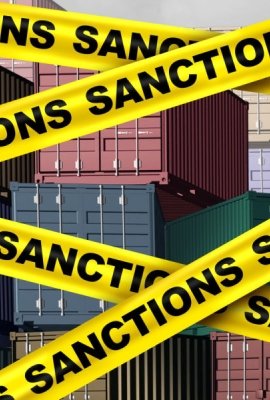 An image of cargo containers with yellow tape that says sanctions over top of them.