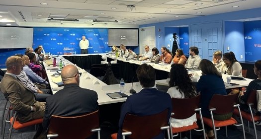 Room filled with people seated at a table with a speaker at the front, on the screens it says AI 101