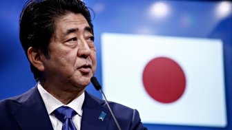 Prime Minister Shinzo Abe speaks in front of a Japanese flag at an event.