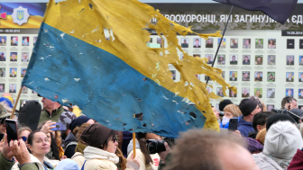 a tattered Ukrainian flag flies above a crowd of people