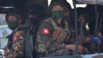 Soldiers in uniforms and masks sitting on a truck.