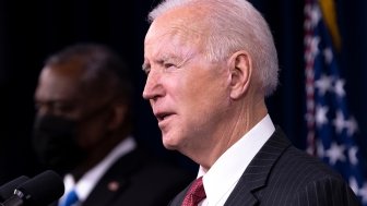 President Biden speaks at a lecturn in front of a background of American flags.