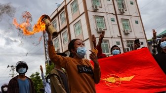 A group of protestors march with the flag of the National League for Democracy, one of them is carrying a lit torch.