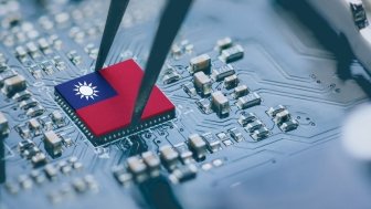 A circuit board with a pair of tweezers placing a part on the board, the part has the map of Taiwan on it.