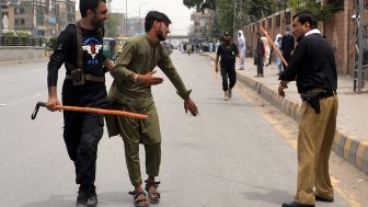 Two men with weapons are detaining another man on the street as people look on.