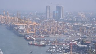 An aerial view of a port with cranes, ships, and skyscrapers.