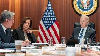 Secretary Blinken, Vice President Harris, and President Biden sit at a table while having a discussion.