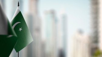 Two small Pakistani flags on a table with an out of focus city skyline in the background.