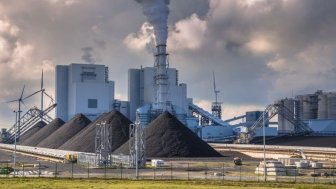 A large power plant with piles of coal outside of the buildings.