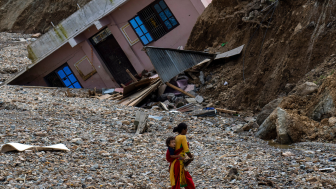 A woman with a child on her back walks past a house which had collapsed due to flooding in the Nakhu river caused by heavy rains in Lalitpur, Nepal, on Tuesday, October 1, 2024. AP Photo/Niranjan Shrestha.