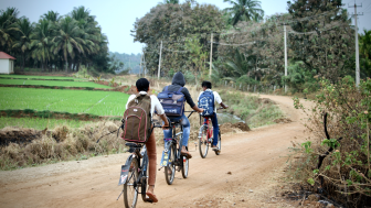 South Indian village children(friends) are going to school by bicycles(cycles or bikes) on a mud road in a nearby village