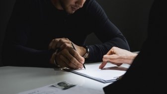  man with handcuffs signing a document in interrogation room