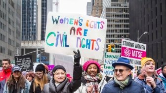 Group of people walking together – sign reads “Women’s Rights are Civil Rights” in Midtown Manhattan during the NYC Women’s March – New York, NY, USA January 1/19/2019 Women’s March.