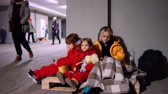 group of little kids, siblings sitting quietly on wooden pallet on the floor in bomb proof shelter during air-raid attack