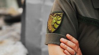 Ukrainian military woman with the lgbt chevron in her hands on the background of an exploded house