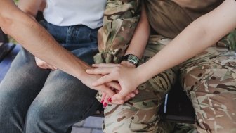 Group holding hands with a uniformed service member in camouflage.. 