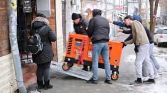 Group of men bringing an orange generator through a doorway