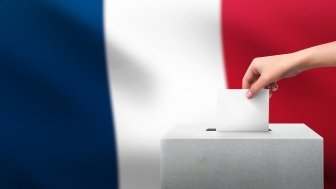 Hand putting a vote into a ballot box in front of the French flag