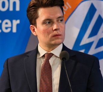 A photo of Lucas Myers speaking at a conference with the Wilson Center logo in the background.